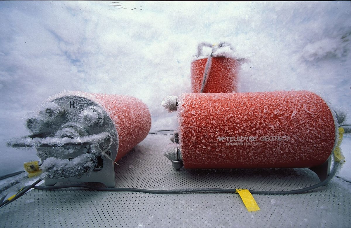 Three orange seismometer cylinders coated in frost inside an ice vault in Antarctica